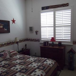 A bedroom with patriotic-themed decor featuring a bed, window shutters, and wall art.