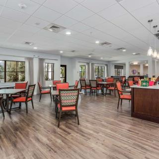 A modern dining area with wooden floors and red-cushioned chairs around multiple tables.