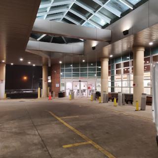 A nighttime view of a building entrance with modern architecture, featuring prominent lighting and a spacious parking area.