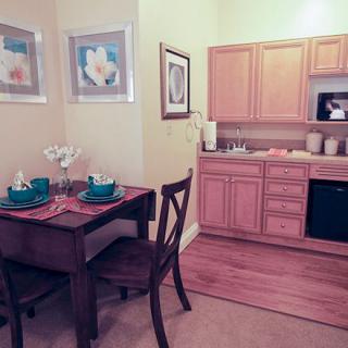 A cozy kitchen and dining area featuring a wooden table set for two, with light wood cabinets and decorative wall art.