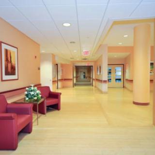 A spacious and clean hospital hallway with red chairs and bright lighting.