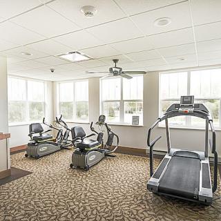 A well-lit gym with exercise equipment, including a treadmill and stationary bikes.