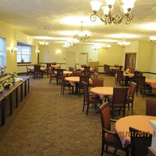 An elegant dining room with neatly arranged tables and chairs, illuminated by chandeliers.