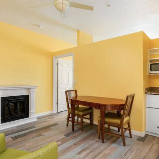A cozy living room with yellow walls featuring a dining table and chairs, a fireplace, and an adjacent kitchen area.