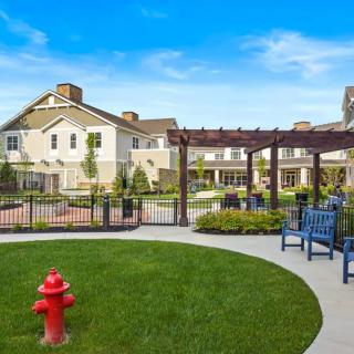 A beautifully landscaped outdoor area with benches, a pergola, and a fire hydrant in front of a large building.