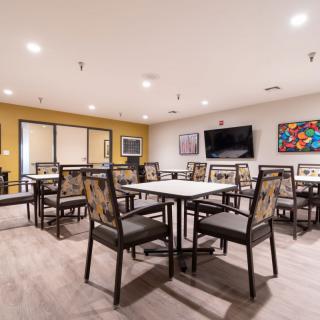 A modern dining area with neatly arranged tables and chairs, displaying artwork on the walls and a television.