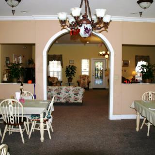 A cozy interior with a dining and living area separated by an archway, featuring elegant chandeliers and classic furniture.