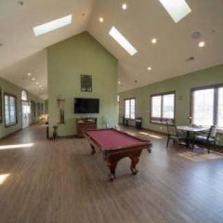 A spacious room featuring a pool table, vaulted ceilings with skylights, and large windows providing ample natural light.