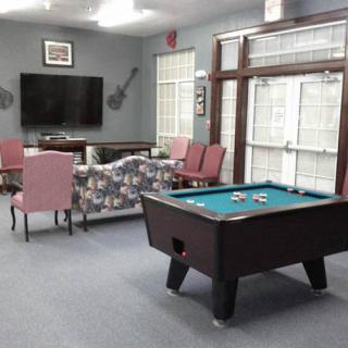 A cozy game room featuring a pool table, television, seating area with chairs and a couch, and large windows.