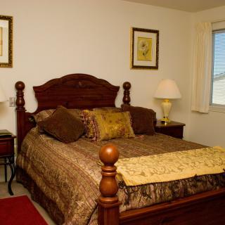 A cozy bedroom featuring a wooden bed with decorative pillows and a matching lamp on the bedside table.