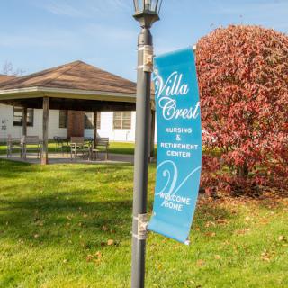 A banner reading 'Villa Crest' is attached to a lamppost, with a building and autumn foliage in the background.