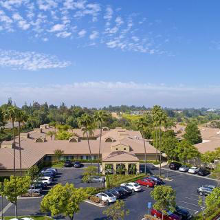 Aerial view of a suburban area with a parking lot surrounded by buildings and lush greenery under a clear blue sky.