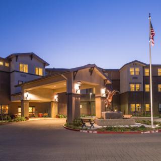 A well-lit hotel exterior at dusk with an entrance and a flagpole.