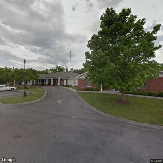 A view of a brick building with a driveway, surrounded by trees under a cloudy sky.