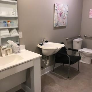 A tidy bathroom with a sink, toilet, and a chair next to shelves holding towels.
