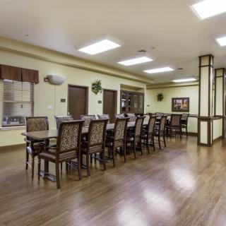 A spacious dining room with a long table and chairs, featuring a wooden floor and bright lighting.