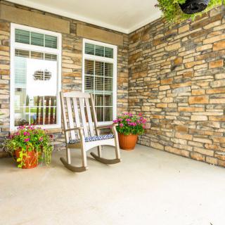 A cozy porch with a rocking chair and potted plants against a stone wall.