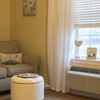 A cozy living room corner featuring an armchair, ottoman, and window with curtains.