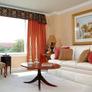 A cozy living room with a white sofa, wooden coffee table, orange curtains, and decorative cushions.