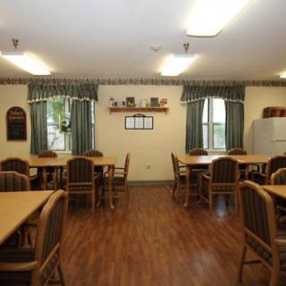 A cozy dining area with tables and chairs, featuring natural lighting and green curtains.
