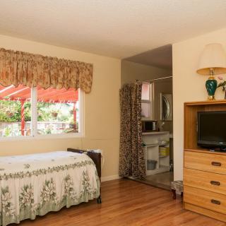 A cozy bedroom featuring a bed, TV, and dresser with a view of the outside through a window.