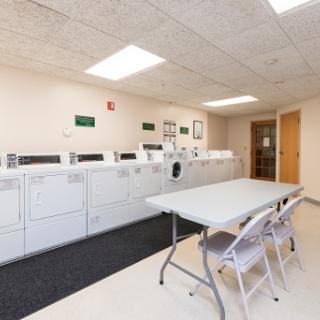 A clean and organized laundry room equipped with washing machines and dryers, along with a table and chairs for convenience.