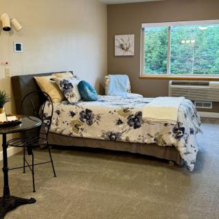 A cozy bedroom with a bed featuring floral bedding, a small round side table, and a window providing natural light.