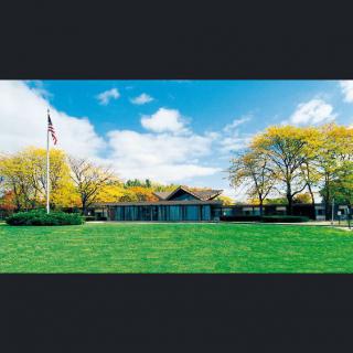 A scenic view of a building surrounded by vibrant green grass and trees under a partly cloudy sky, with a flagpole standing nearby.