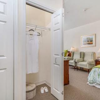 A hotel room featuring a small closet with a bathrobe and slippers, alongside elegant furniture and decor.