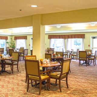 A spacious dining area with neatly arranged tables and chairs, featuring warm lighting and a carpeted floor.