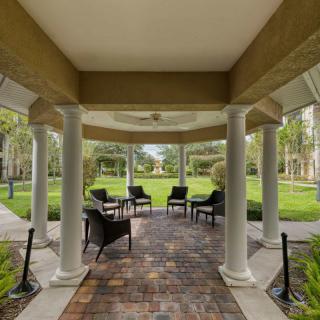A covered patio with columns and outdoor seating overlooking a garden.