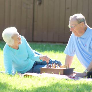 An elderly couple enjoys a game of chess on a sunny day in the park.