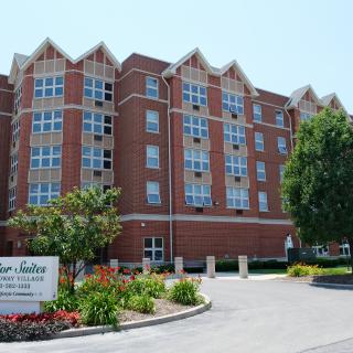 A multi-story brick building with a garden and trees at the entrance.