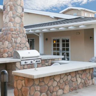 A stylish outdoor kitchen with a stone design features a grill and a spacious patio area.