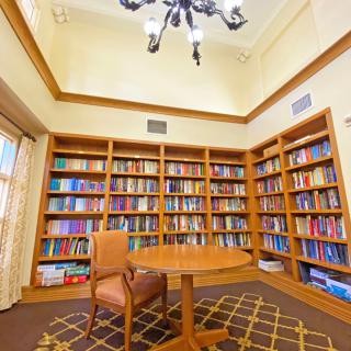 A cozy library corner with wooden bookshelves, a round table, and a comfortable chair.