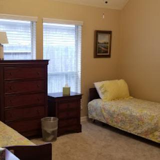 A cozy bedroom featuring a single bed, dresser, and natural light from the windows.