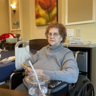 An elderly woman sitting in a wheelchair in a comfortable indoor setting.