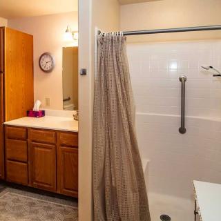A bathroom with a shower and curtain, featuring a vanity with a sink, mirror, cabinets, and a wall clock.