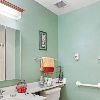 A neatly organized bathroom with green walls, featuring a sink, mirror, and towels.