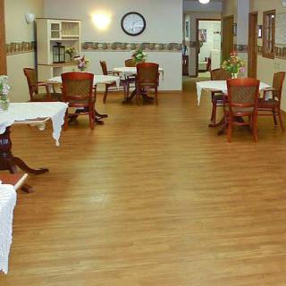 An empty dining area with wooden flooring, featuring arranged tables and chairs.