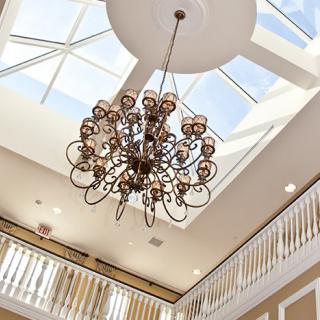 A luxurious chandelier hanging from a ceiling with a skylight above.