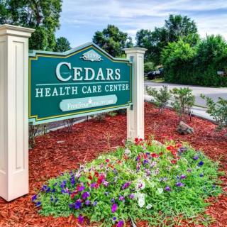 Entrance sign for Cedars Health Care Center with colorful flower bed.