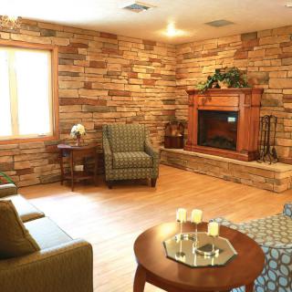 A cozy living room with wooden walls and a fireplace, featuring comfortable seating and natural light.
