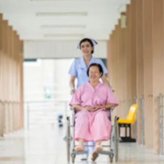 A nurse pushes a patient in a wheelchair down a hospital corridor.