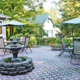 A tranquil patio with outdoor seating, surrounded by a lush garden, featuring a decorative stone fountain.