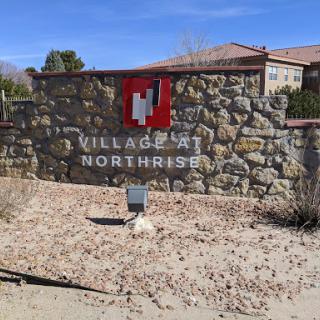 Entrance sign for the Villages at Northrise, featuring a stone wall and clear blue sky.