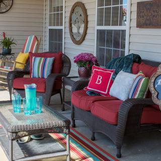 A cozy outdoor patio setup with armchairs, colorful cushions, and a small table surrounded by decorative items and plants.