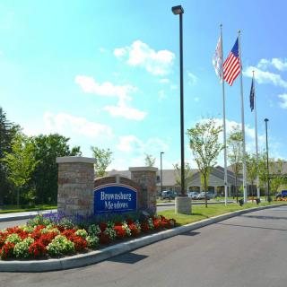 Entrance of a facility with a welcoming sign, flags, and landscaped flowers.