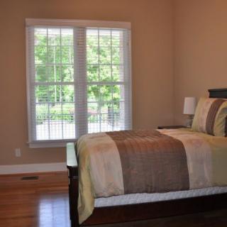 A cozy bedroom with a neatly made bed and large window allowing natural light to enter.
