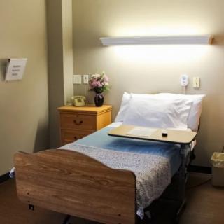 A well-lit hospital room with a single bed and wooden furniture.